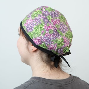 May include: A black and green patterned surgical scrub cap with a black tie. The cap has a grape design.