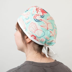 May include: A light blue surgical scrub cap with a white trim and a pattern of medical tools in red and white.