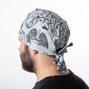 Puede incluir: Un gorro de quirófano gris con un estampado anatómico en blanco y negro de un cerebro, un corazón y unos pulmones.