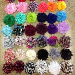 May include: Assortment of 36 handmade fabric flowers in various colors and patterns. The flowers are arranged in rows on a light brown surface.