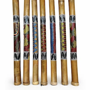 May include: Seven bamboo didgeridoos with colorful, patterned bands. The bands feature dot art in red, yellow, blue, and white. The didgeridoos are arranged vertically against a white background.