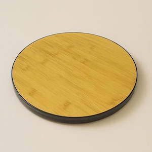 Puede incluir: Una bandeja redonda de bambú con borde negro. La bandeja presenta un patrón de vetas de madera natural y es adecuada para servir alimentos o exhibir objetos decorativos. La bandeja tiene aproximadamente 25 cm de diámetro.