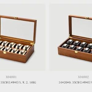 Puede incluir: Dos cajas de madera para relojes con tapas de cristal. Una caja contiene diez relojes con correas blancas y negras, la otra diez relojes con correas negras. Las cajas están etiquetadas X04801 y X04802.