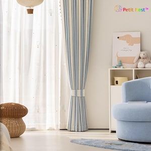May include: A light blue and white striped curtain is tied back with a matching band. Sheer white curtains with a hot air balloon pattern are visible behind the striped curtain. A light blue armchair and a decorative mushroom-shaped basket are in the foreground.
