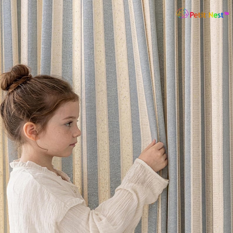 May include: Striped curtains in shades of blue, beige, and white. The vertical stripes create a classic, clean look. The fabric appears to be a textured linen or cotton blend. The curtains are partially drawn, revealing the texture and color variations.