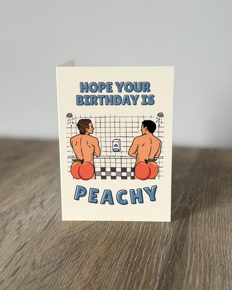 May include: Greeting card with the text "HOPE YOUR BIRTHDAY IS PEACHY". The card features a cartoon illustration of two men in a shower with peach-shaped bottoms. The background is a grid pattern.