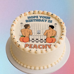 May include: A round, frosted cake with a decorative border. The cake features an image of two cartoon figures with peach-shaped bottoms in a shower scene. The text "HOPE YOUR BIRTHDAY IS PEACHY" is displayed on the cake.