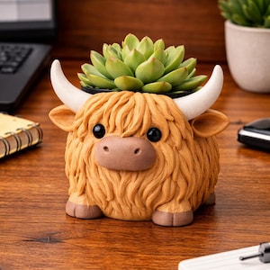 May include: A planter shaped like a Highland cow with shaggy golden-brown fur, a smooth tan muzzle, and two curved white horns. The cow has large black eyes and small brown hooves. A green succulent plant is potted inside the top of the planter.