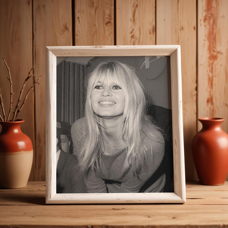 May include: A rectangular picture frame with a distressed white finish containing a black and white photograph of a smiling person with long blonde hair and bangs. The frame is positioned upright, showcasing a classic portrait style.