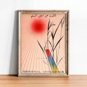 May include: A framed poster featuring a red sun with radiating lines on a light peach background. Black silhouettes of tall grass stalks are in the foreground. A rainbow-coloured rectangular bar sits behind the grass. Text reads General Dynamics.