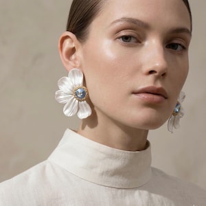 Puede incluir: Una taza de cerámica blanca con un asa negra y el texto "But First, Coffee" en un estilo manuscrito. La taza está sobre una superficie blanca. La taza mide aproximadamente 10 cm de alto.