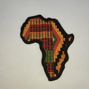 May include: A black fabric outline of the continent of Africa with a colorful patterned fabric inside. The pattern is a mix of yellow, red, green, and black.