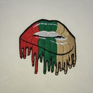May include: A red, green, and gold embroidered patch shaped like a dripping pair of lips.
