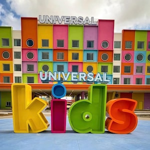 May include: A large, colorful, three-dimensional sign spelling out the word 'kids' in yellow, pink, green, and orange letters stands in front of a building with a grid of bright, multi-colored square and circular windows labeled 'UNIVERSAL'.