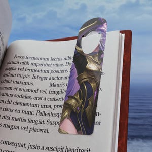Puede incluir: Un marcapáginas con una ilustración de personaje con detalles en morado y dorado. El marcapáginas está insertado en un libro con texto visible en las páginas. El fondo muestra un cielo azul con nubes.