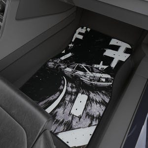 Op de afbeelding: Zwart-witte auto vloermat met een gestileerde afbeelding van een auto die op een weg racet. De rechthoekige mat, met Japanse karakters, is ontworpen voor de binnenkant van een auto.