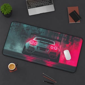 May include: A black rectangular desk mat featuring a stylized image of a silver sports car with red taillights and exhaust pipes. The car is set against a backdrop of teal and red hues, with a white computer mouse on the right.