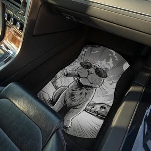 May include: Black and white car floor mat featuring a cool cat wearing sunglasses and smoking a cigar. The cat is in a car with a vintage camper in the background. The mat is designed to fit in a car.