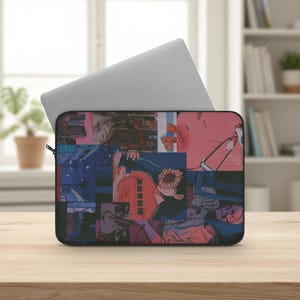 Puede incluir: Una funda negra para portátil con un collage de ilustraciones de estilo anime en tonos rosa, azul y naranja. Un portátil plateado está parcialmente insertado. La funda está sobre una superficie de madera.