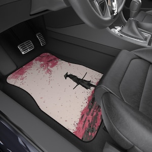 Puede incluir: Alfombrilla para el suelo del coche con un diseño de samurái japonés, sobre un fondo de flores de cerezo rosas y un fondo beige claro. La alfombrilla tiene un borde negro y está colocada en un coche.