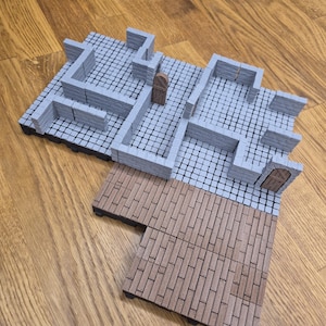 Puede incluir: Un conjunto de terreno de mazmorra en miniatura gris con paredes de piedra, una puerta de madera marrón y un suelo de madera marrón. El conjunto está diseñado para juegos de mesa y juegos de rol.