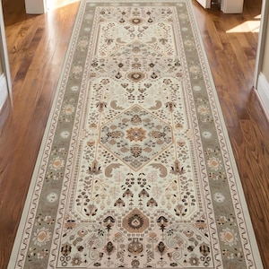 May include: A long rectangular runner rug featuring a cream-coloured centre with intricate floral and geometric patterns in shades of brown, tan, and muted blue. The rug has a wide, decorative border with repeating floral motifs in similar tones.