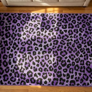 May include: A rectangular area rug with a purple leopard print pattern. The rug features black spots on a purple background, creating a bold and stylish design. The rug is placed on a hardwood floor.