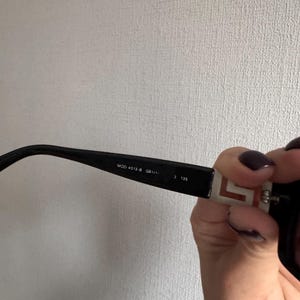 May include: Black sunglasses with a rectangular frame. The arm of the glasses has the text "MOD 4013-B GB1/11" and "3 135". The arm also has a white and red design.