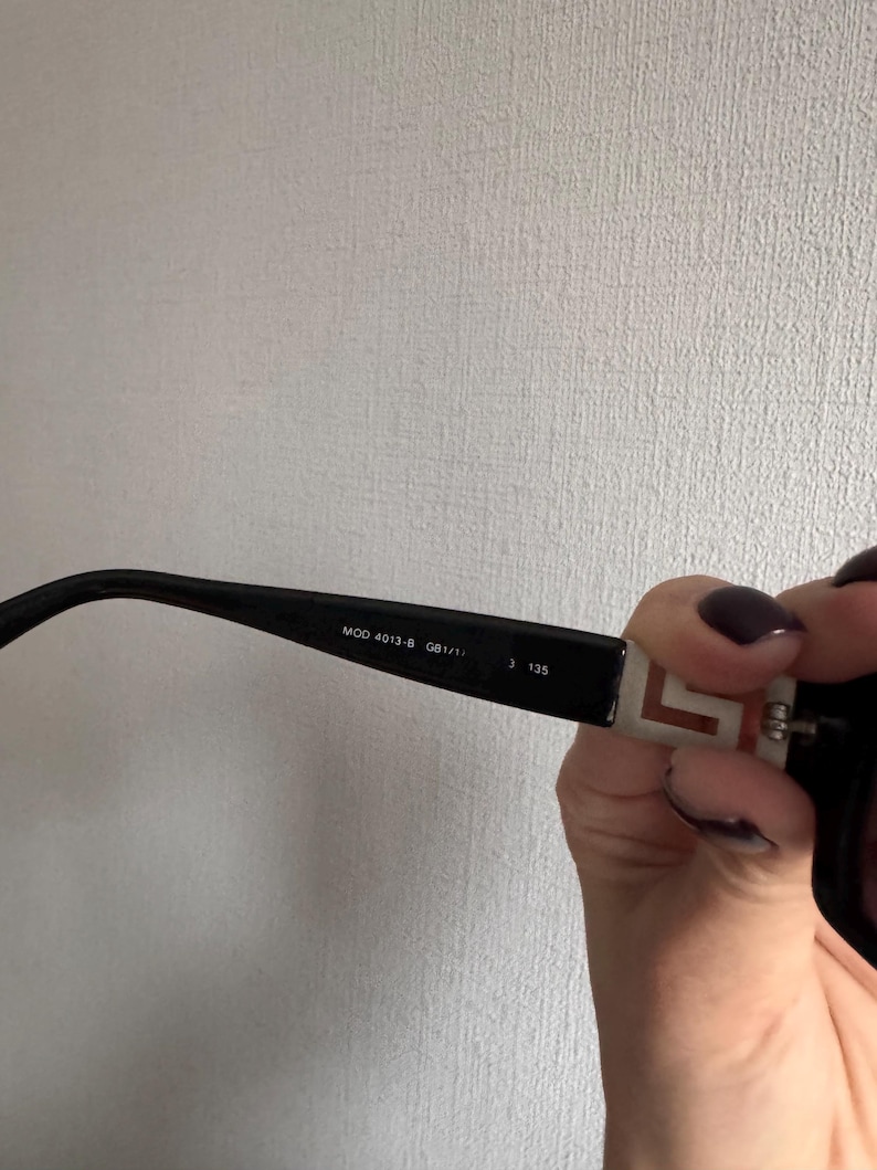 May include: Black sunglasses with a rectangular frame. The arm of the glasses has the text "MOD 4013-B GB1/11" and "3 135". The arm also has a white and red design.