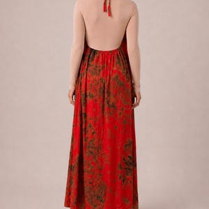 May include: A floor-length dress featuring a vibrant red skirt with a dark green mottled pattern and a beige long-sleeved bodice. The garment has an open back design with a halter-style tie closure at the neck, showcasing a flowing silhouette.