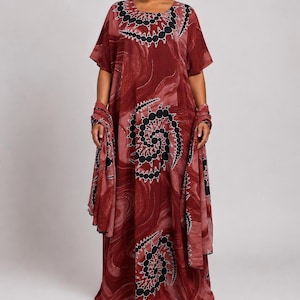 May include: A floor-length kaftan dress in deep burgundy with a swirling marble-like pattern. The garment features a round neckline and short sleeves, accented by black and white spiral motifs. A matching long scarf is draped over the arms.