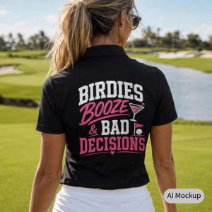 May include: A black polo shirt featuring white and pink text on the back that reads "BIRDIES BOOZE & BAD DECISIONS" with a graphic of a martini glass and a golf ball on a tee. The shirt has a collar and short sleeves, worn over white bottoms.