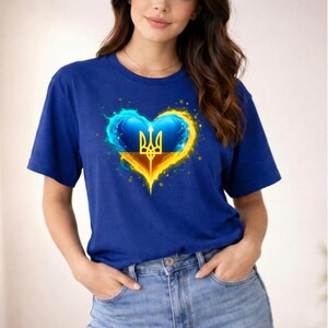 May include: A royal blue t-shirt featuring a heart-shaped design with the Ukrainian coat of arms. The heart is a mix of blue and yellow, with a glowing effect. The shirt has short sleeves and a crew neck.