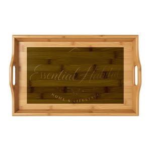 Peut inclure: Plateau de service rectangulaire en bambou avec poignées découpées. Le plateau présente un centre marron foncé avec les mots "Essential Habitat" et "Home & Lifestyle" en écriture claire. Le cadre extérieur est de couleur marron clair.