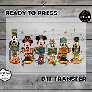 May include: A DTF transfer sheet featuring cartoon characters dressed as nutcrackers, including Goofy, Minnie Mouse, Mickey Mouse, Daisy Duck, Donald Duck, and Pluto. The design includes colorful Christmas lights, snowflakes, and stars.