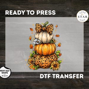 May include: A DTF transfer featuring a stack of three pumpkins with a leopard print bow on the top pumpkin, surrounded by autumn leaves and flowers. The text reads READY TO PRESS, LONE STAR GIFT, and DTF TRANSFER. The design has a white background.