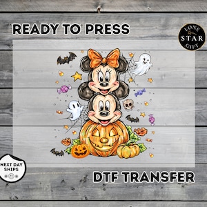May include: A Halloween-themed DTF transfer featuring a stacked illustration of two cartoon mice, one wearing an orange bow, sitting atop a large jack-o'-lantern. The design includes ghosts, bats, candy corn, skulls, and autumn leaves.