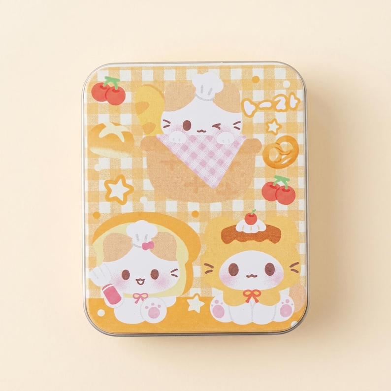 May include: Rectangular tin with a yellow gingham pattern and cartoon illustrations of cats dressed as baked goods. The tin features images of a cat in a bread bowl, a cat on toast, and a cat in a pastry.