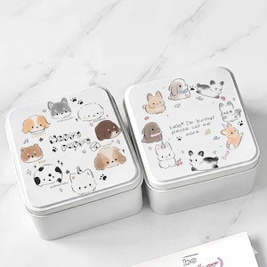 May include: Two white metal boxes with lids featuring cartoon dog and bunny illustrations. One box says "Happy Puppy" with various dog breeds. The other says "hello I'm bunny! please call me more".