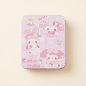 May include: A rectangular pink tin featuring cartoon characters in winter attire. The tin has a light pink background with illustrations of characters wearing hats and bows. The text "Hello-" and "Snow flake" are also visible.