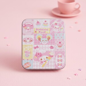 May include: A rectangular pink tin with a patchwork design featuring cartoon characters, cupcakes, and the words "Delicious Food." The tin is decorated with various pink and white patterns and illustrations, with a pink teacup and saucer in the background.