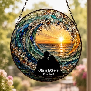 May include: A circular stained glass suncatcher featuring a wave design in shades of blue and teal, framing a sunset over the ocean. A silhouette of two people is at the bottom with the text Oliver & Clara and the date 26.06.23 printed in white.