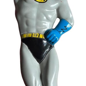 May include: A figurine of Batman in a dynamic pose, featuring a gray body, black trunks, and blue accents on the cape, gloves, and boots. The iconic yellow bat symbol is on the chest. The figure is approximately 6 inches tall.