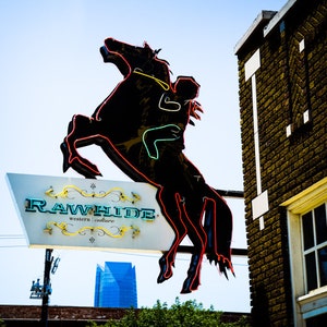 May include: A neon sign with a black silhouette of a horse rearing up on its hind legs. The sign says "Rawhide Western Culture" in yellow and green neon letters.