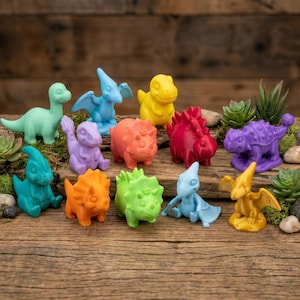 May include: A collection of colorful dinosaur figurines in various poses. The dinosaurs are in shades of green, blue, yellow, orange, red, and purple. They are arranged on a wooden surface with small plants and rocks.