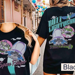 May include: A black t-shirt featuring a graphic print of Buzz Lightyear, a spaceship, and the text "Buzz Lightyear" and "Space Ranger". The design includes a circular pink background, a planet icon, and stylized lettering in shades of blue and purple.