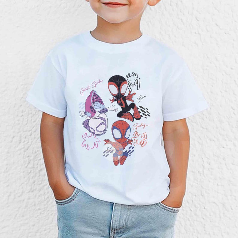 Op de afbeelding: Wit T-shirt met cartoon illustraties van Spider-Man personages, waaronder Ghost Spider en Spider-Man. Het ontwerp bevat de namen van de personages in een handschrift. Het T-shirt wordt door een kind gedragen.