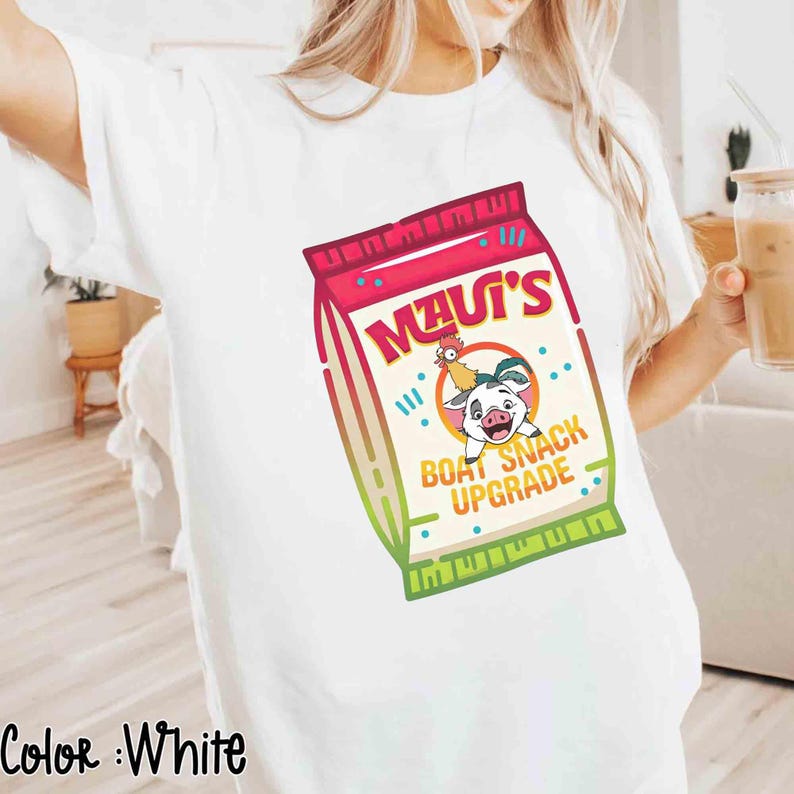 Puede incluir: Camiseta blanca con un gr&aacute;fico colorido de una bolsa de snacks con el texto "Maui's Boat Snack Upgrade" y un cerdo y un gallo de dibujos animados. El gr&aacute;fico utiliza tonos de rojo, rosa, verde y beige.