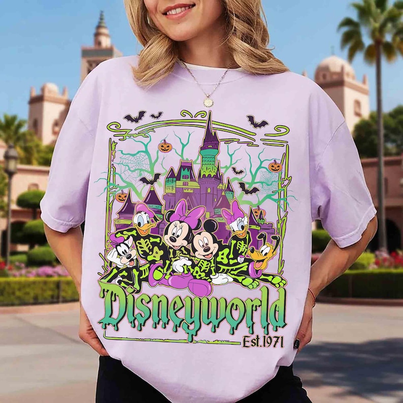 May include: A lilac t-shirt with a Disney World Halloween design. The graphic shows Mickey and Minnie Mouse, Donald and Daisy Duck, and Pluto in skeleton costumes, with a castle and bats. The text "Disneyworld Est. 1971" is displayed below the characters.