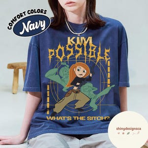 May include: Navy blue t-shirt featuring a graphic of Kim Possible with the text "KIM POSSIBLE" and "WHAT'S THE SITCH?". The shirt has a Comfort Colors label and a design of Kim Possible in action.